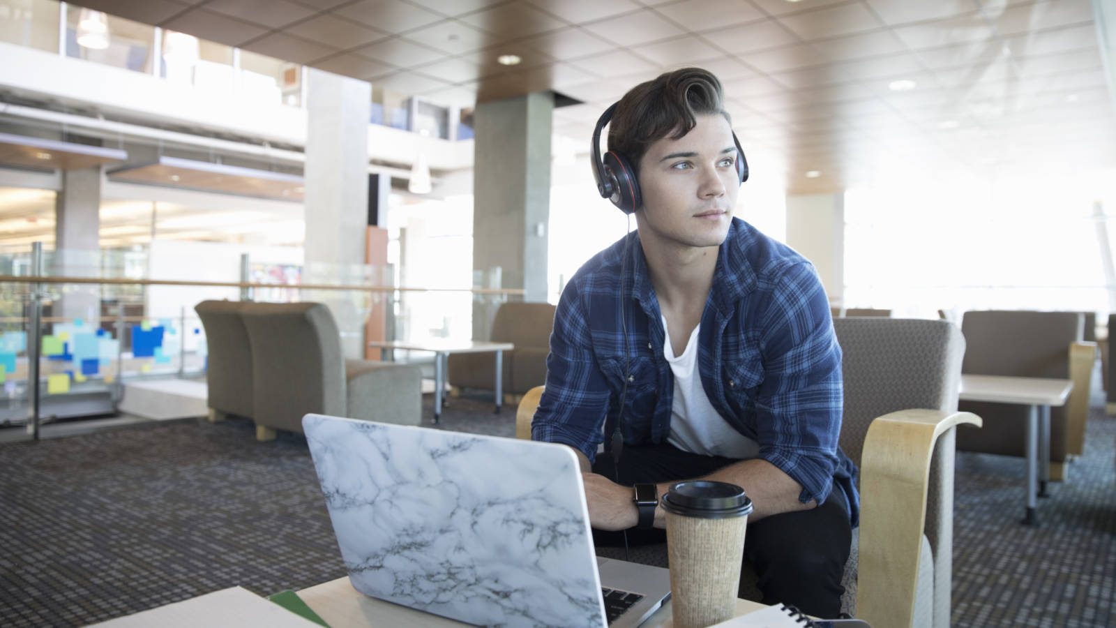 Pensive male college student with headphones listening to music at laptop in student lounge