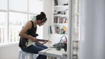 Teenage girl playing electric guitar, recording music in home office