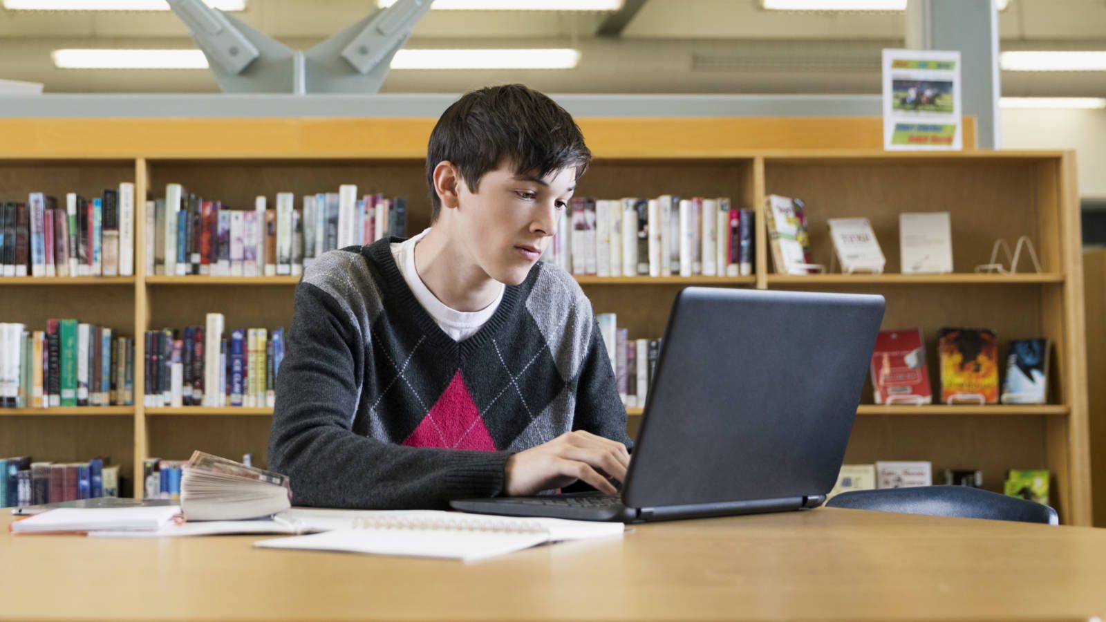Focused high school student using laptop in library