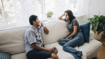 High angle view of father and daughter talking while sitting on sofa by window at home