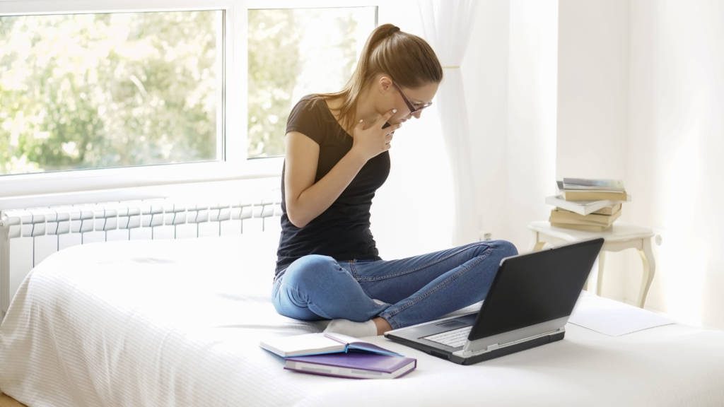 Student sitting on their bed with a laptop researching how to choose a college without visiting it