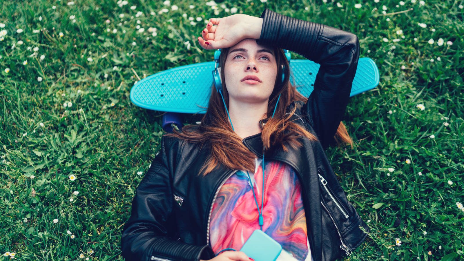 Student listening to music through headphones and laying on a skateboard in the grass