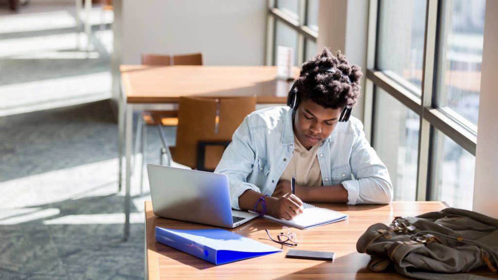 Student studying for AP® exams while wearing headphones and writing in a notebook