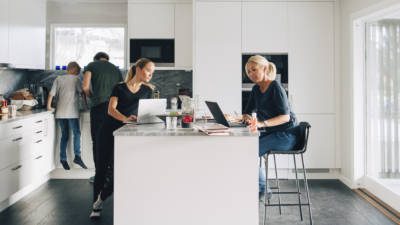 Woman and teenage girl using laptops while man boy standing in kitchen at home