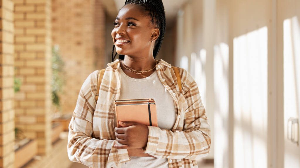 Black woman, college student and thinking about future with books while walking at campus or university. Young gen z female happy about education, learning and choice to study at school building