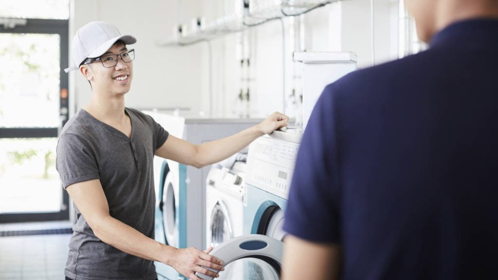 Smiling man talking to university friend while doing laundry