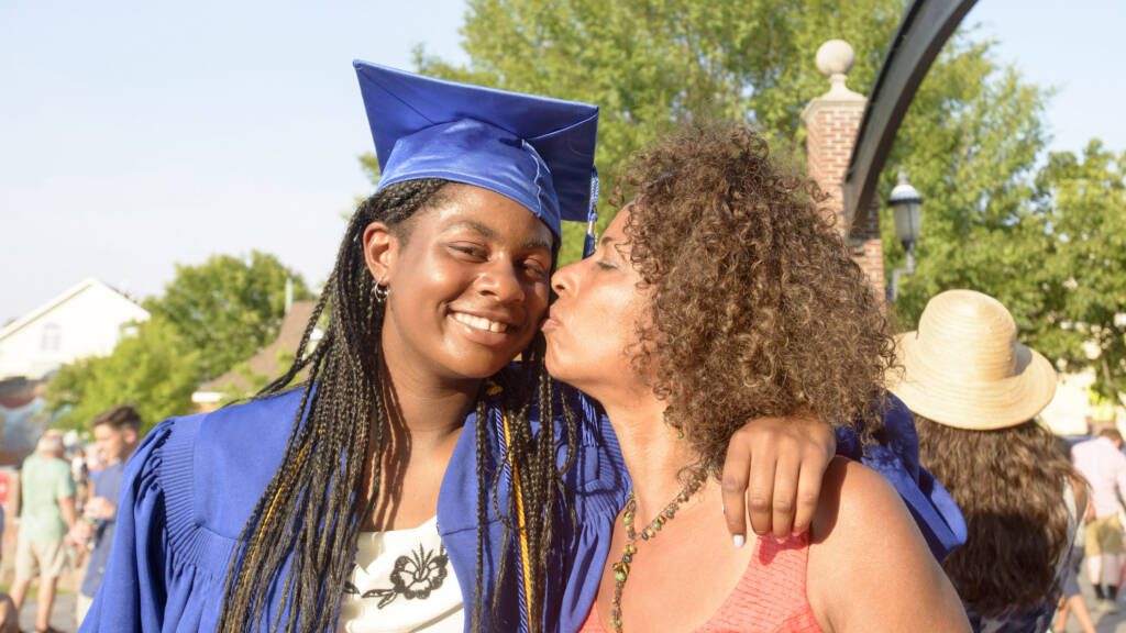 Parent kissing child on the cheek during high school graduation