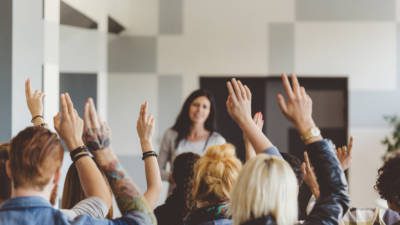 Multiple students raising their hands in a classroom ready to answer their teacher's question