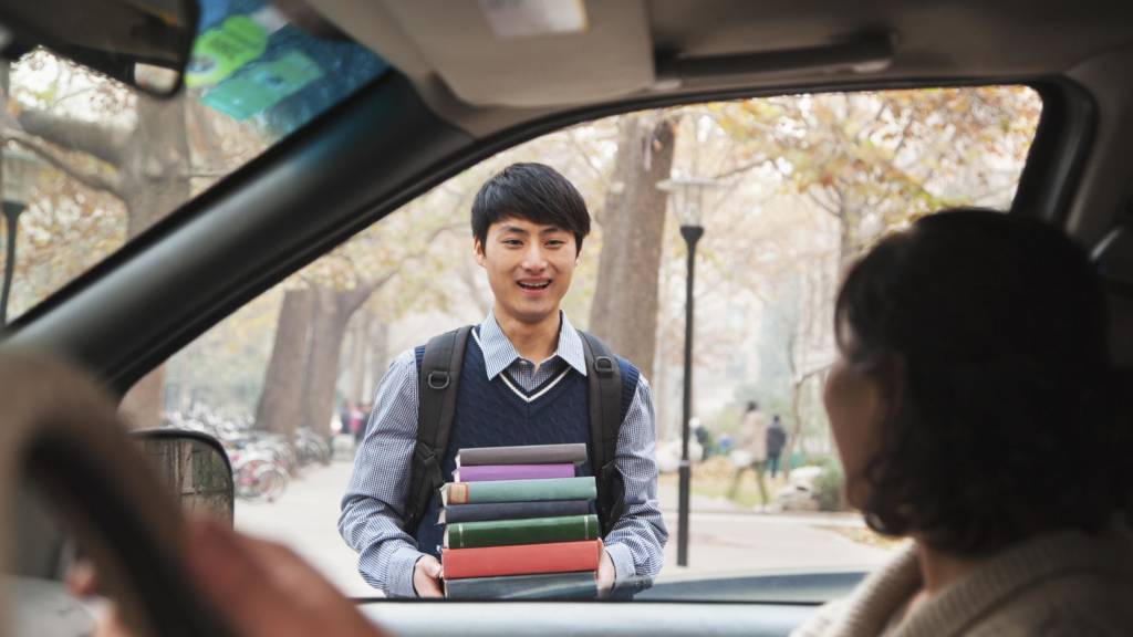 Student holding books while standing outside their parent’s car
