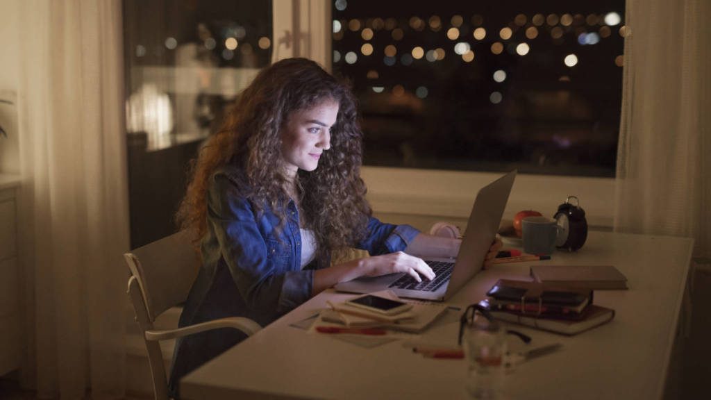 Woman sitting at desk and working on laptop at night.
