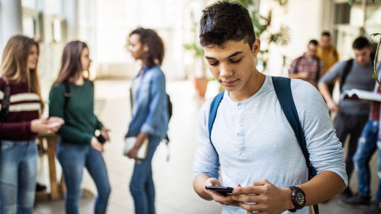 Male high school student using cell phone in a school hallway.